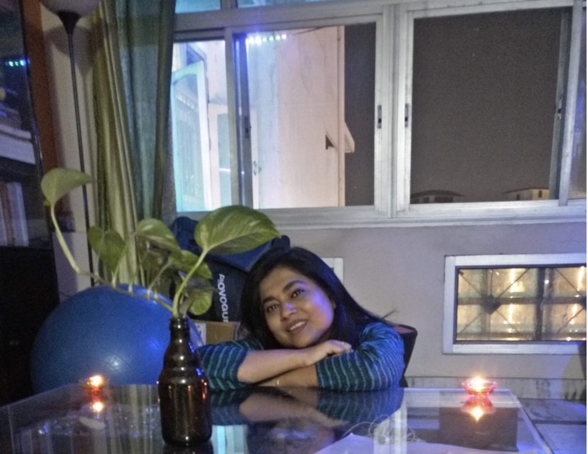 Woman sits at a kitchen table with large windows in the background.