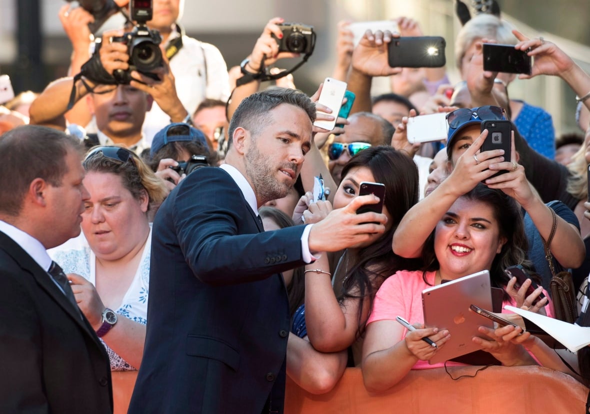 film-tiff-mississppi-grind-20150916 Actor Ryan Reynolds, in a suit, takes selfies with fans on the TIFF red carpet in 2015