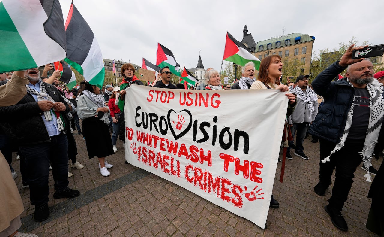 default-319 A crowd of protesters carries a large sign that says "Stop Using Eurovision to Whitewash Israeli Crimes". Many Palestinian flags are visible.