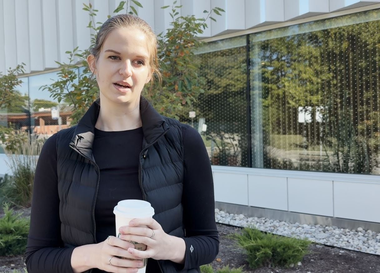 A young woman wearing black holds a coffee cup in her hand.