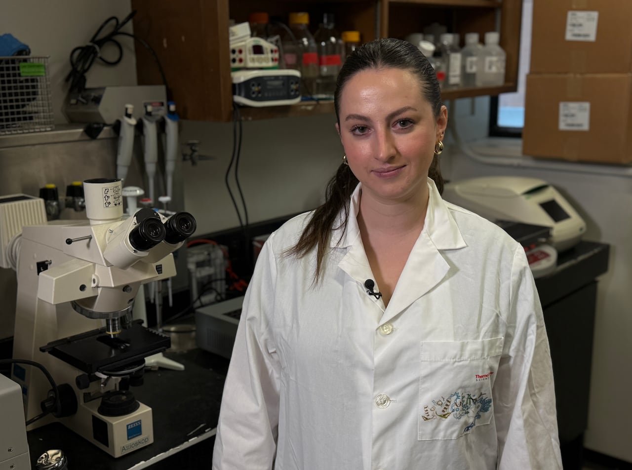 A woman in a lab coat stands beside a microscope.