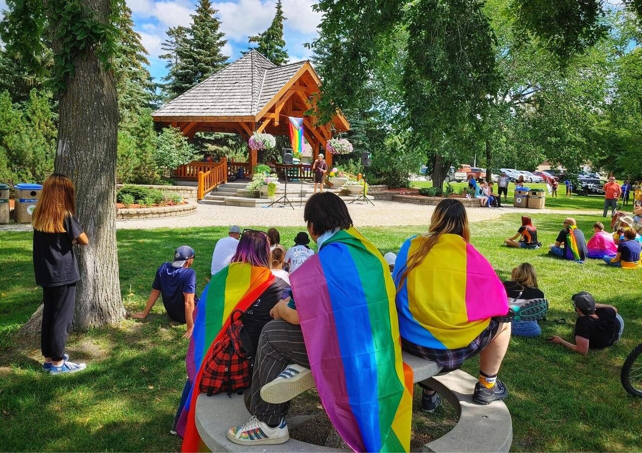 People sitting in a park with Pride flags wrapped around their shoulders.