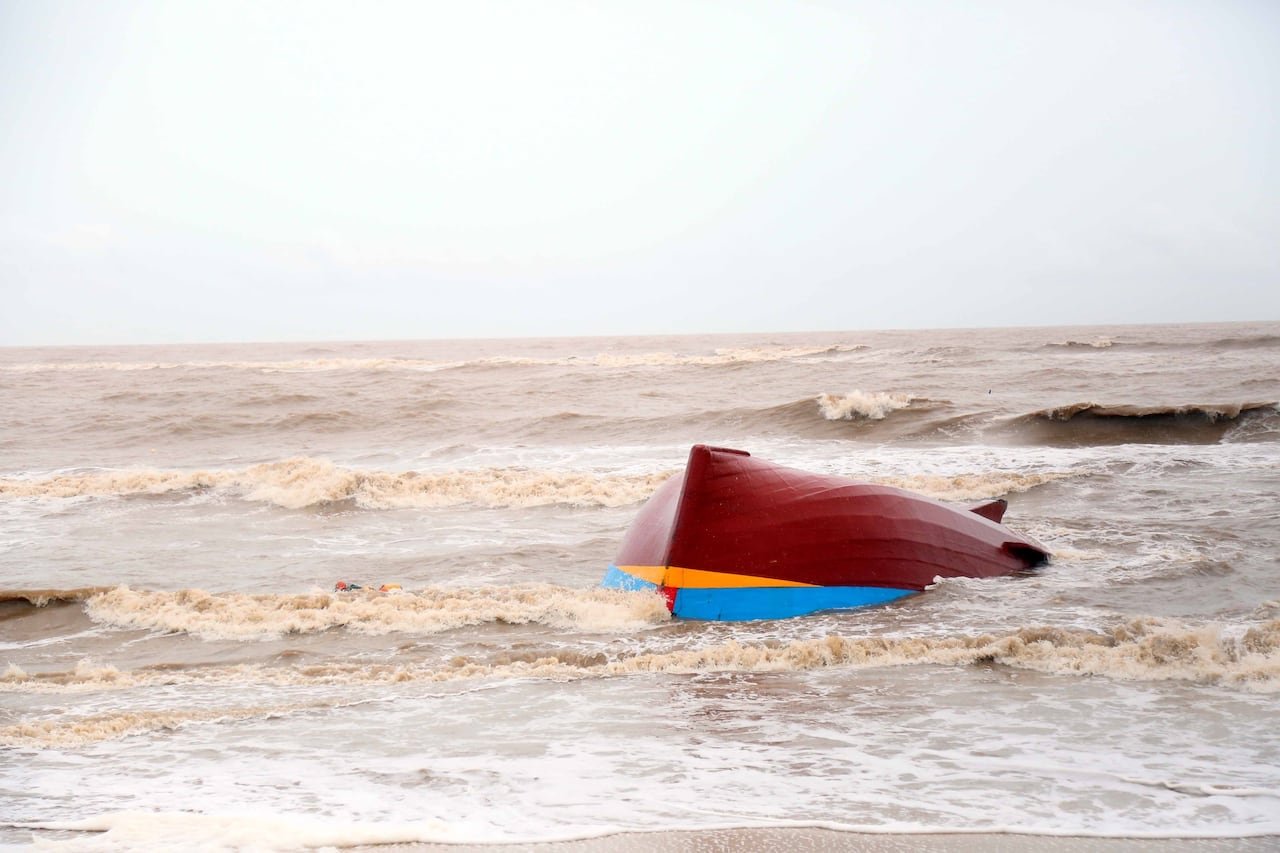 A small red boat is overturned in a body of water with significant waves.