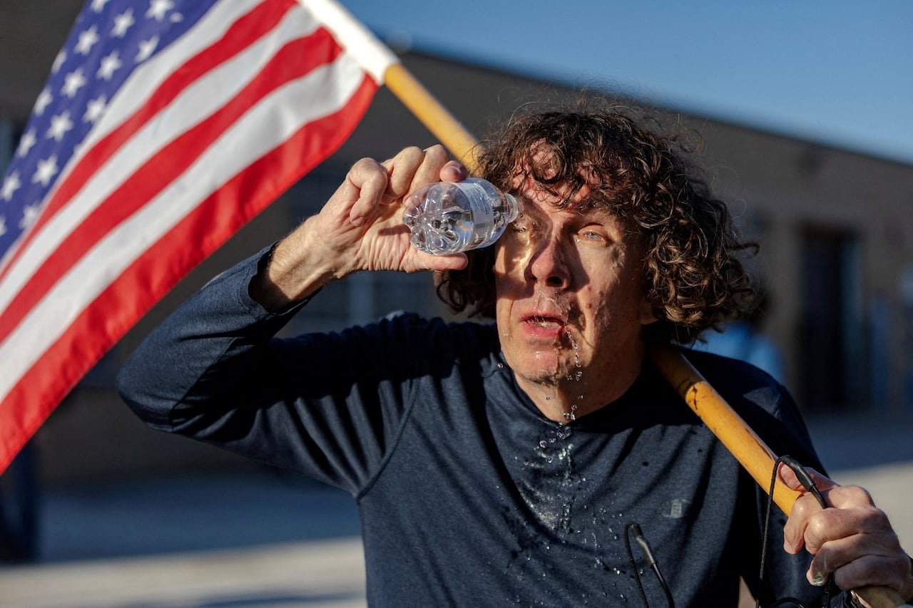 A man flushes a chemical irritant out of his eyes while holding an American flag.