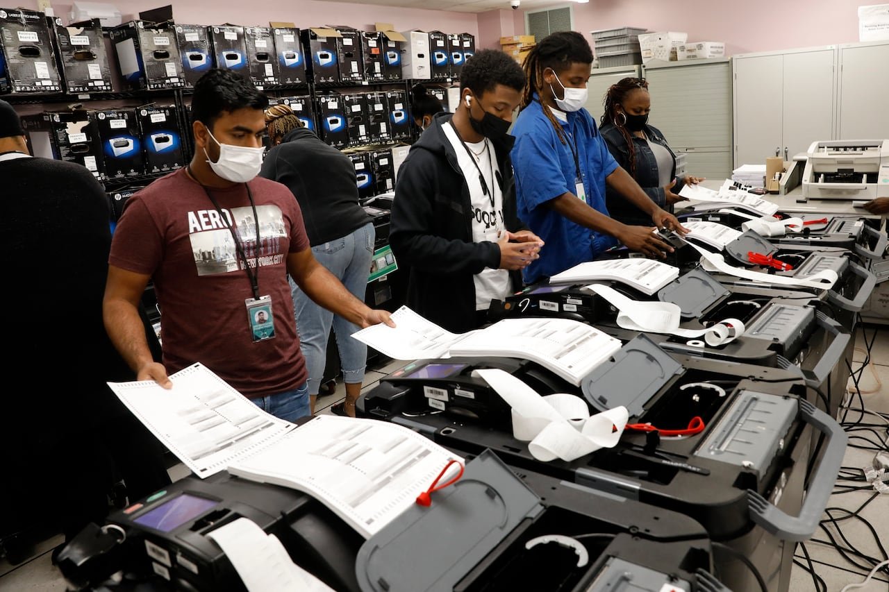 Several people wearing COVID-19 masks use machinery to retrieve printed paper.
