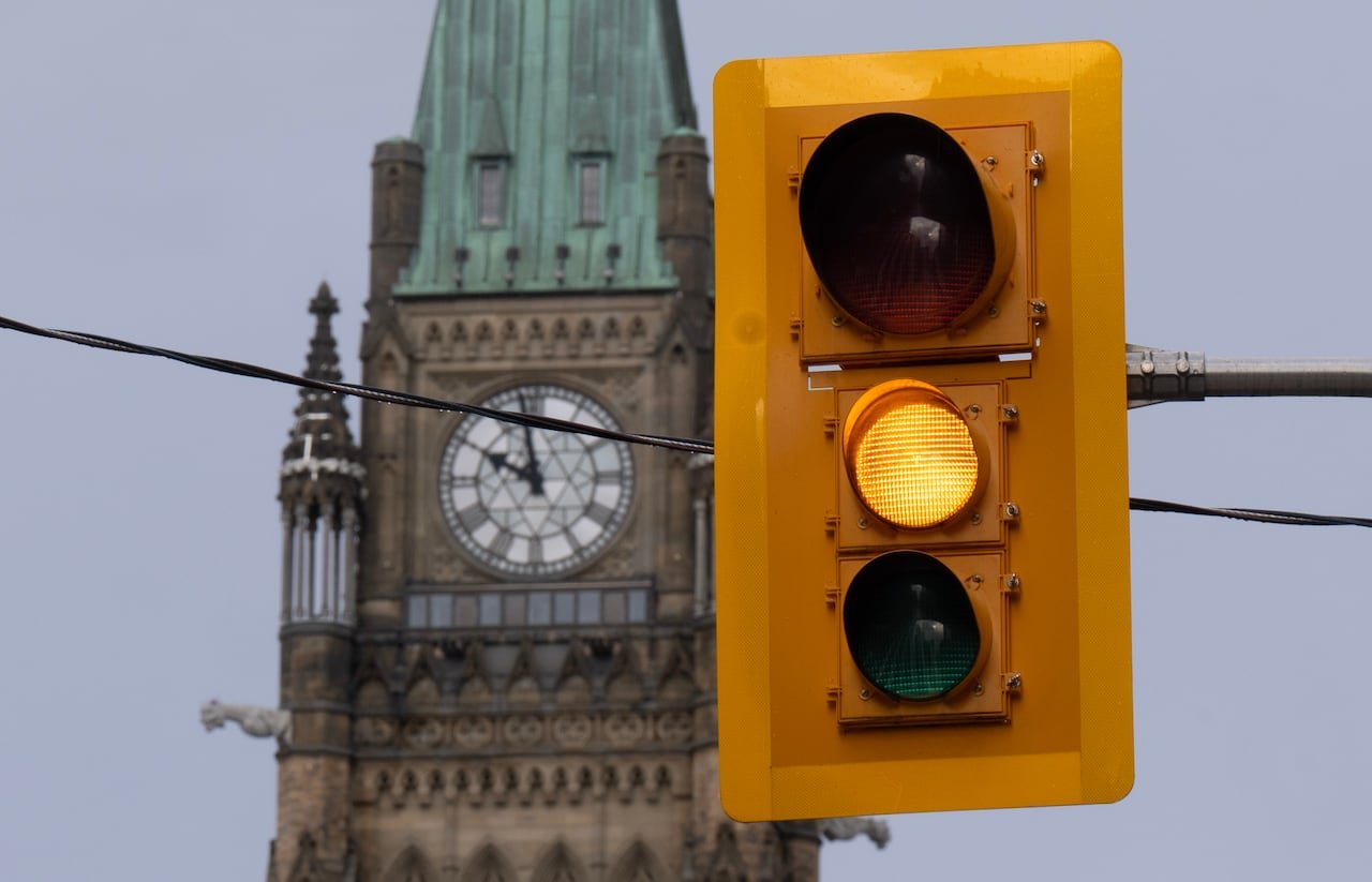 A traffic light is seen up close with a clock tower in the background.