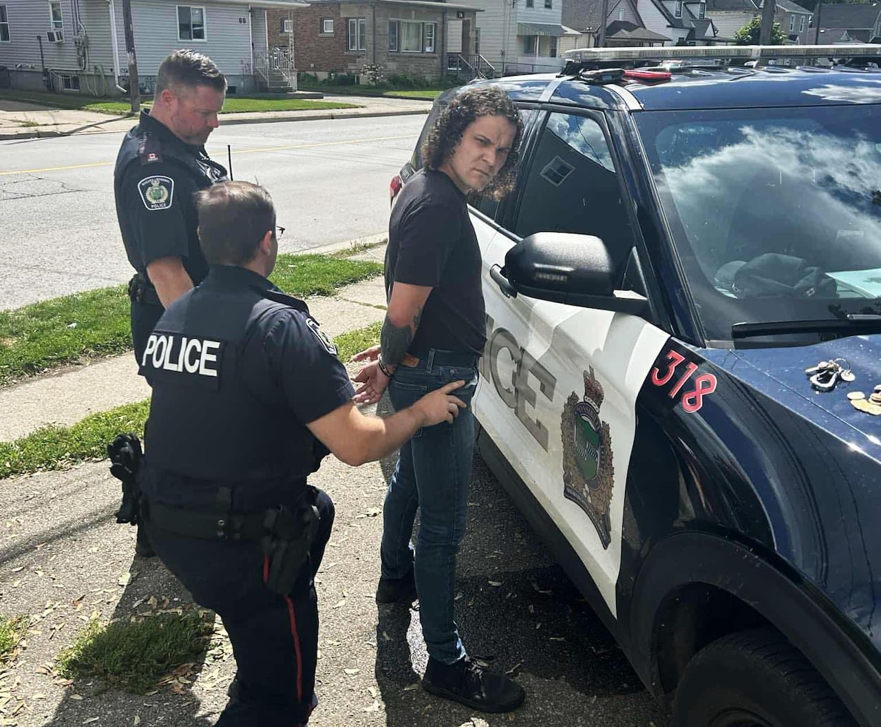 man being handcuffed a police car with two cops behind him