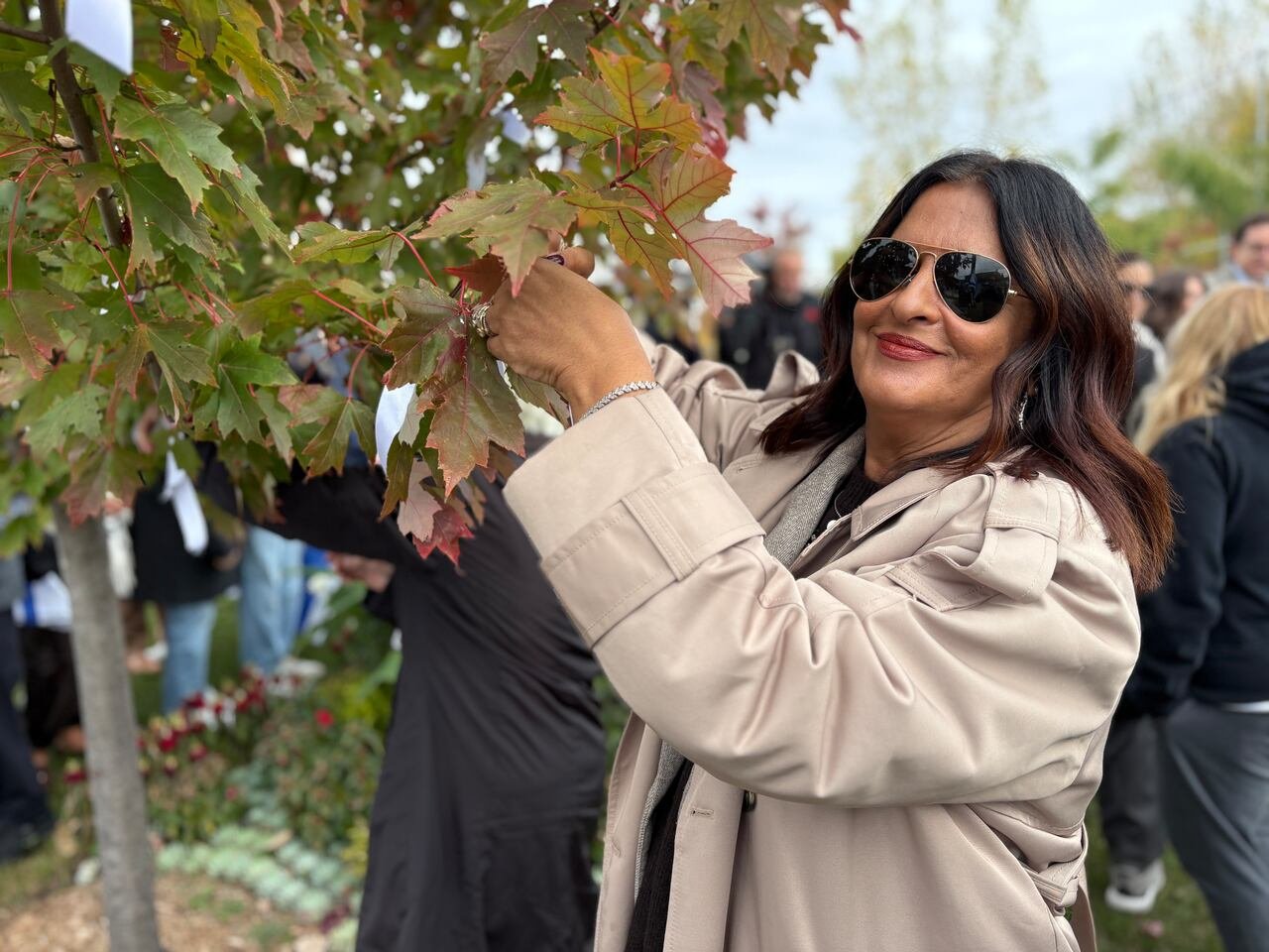 A woman in the foreground ties a white ribbon to a tree.