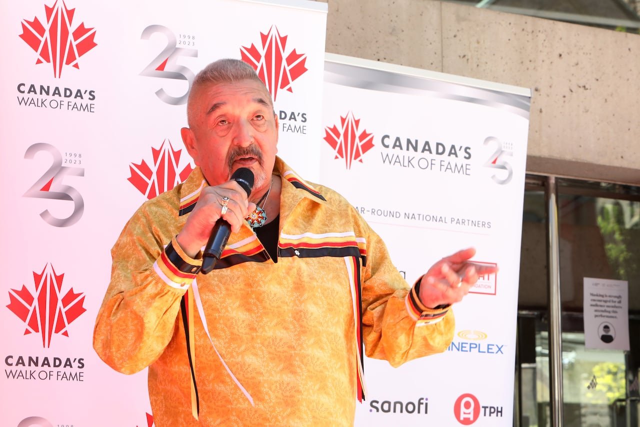 default-314 A man with short cropped grey hair and a mustache is shown speaking into a microphone while speaking at an outdoor event.
