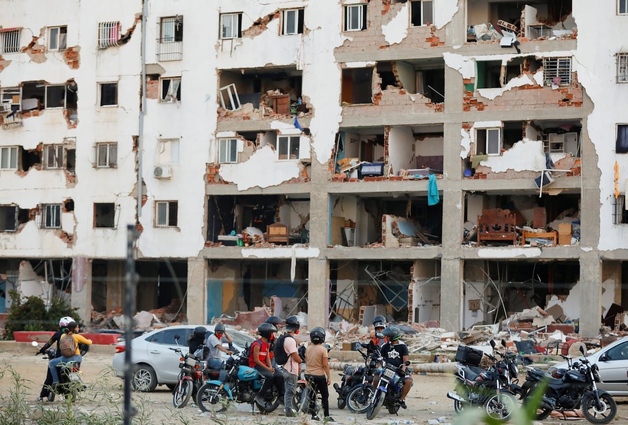 default-356 People in motorcycle helmets look at the remains of a building.